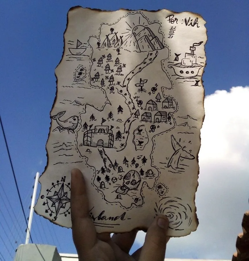 A hand holding up a burnt-edge hand-drawn treasure map against a blue sky, showing islands, mountains, villages, a whale, and a compass rose in pen and ink